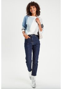 Pull en tricot bleu, gris et blanc avec un design color-block ; jeans foncés taille haute ; bottines argentées ; texture lisse ; coupe décontractée.
