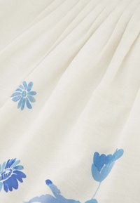 Witte stof met blauwe bloemmotieven, met verschillende bloemvormen. De textuur lijkt zacht met subtiele plooien.