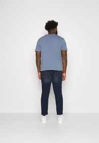 Camiseta azul de manga corta con corte recto, combinada con jeans de mezclilla oscura. El conjunto se completa con zapatillas blancas.