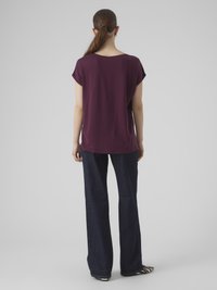 Bordeaux kortermet topp med en avslappet passform, kombinert med mørkeblå vide jeans. Stripete sko synlige nederst.