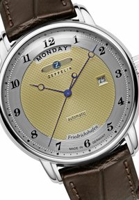 Automatische Uhr mit einem goldfarbenen strukturierten Zifferblatt, silberner Lünette, braunem Lederarmband, blauen Zeigern, Datumsanzeige und Montagindikator auf 12 Uhr.