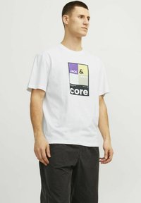 Baltas medvilnės marškinėliai su daugiaspalvėmis grafikomis, ant kurių užrašyta "JACK & JONES" ir "core" priekyje. Trumpomis rankovėmis, laisvas kirpimas.