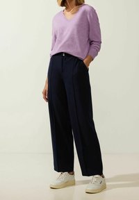 Pull violet clair à col en V associé à un pantalon large bleu marine et des baskets beige. Texture lisse, haut ajusté, design à plis sur le pantalon.