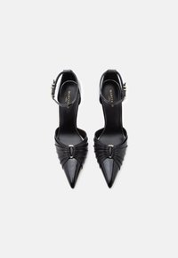 Mustad ja terava ninaga kontsad, millel on pahkluu rihmad, volditud detailid ja kuldsed klambrid valgel taustal.