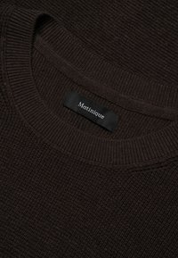 Pull marron texturé avec un col rond côtelé. L'étiquette indique "Matinique". Le matériau semble être en maille avec un motif régulier sur toute la surface.