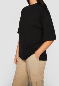 Černé tričko s vysokým výstřihem a krátkými rukávy, doplněné béžovými cargo kalhotami se bočními kapsami a volným střihem.