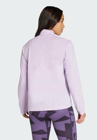 Ljuslila långärmad jacka med hög krage och slät textur. Matchas med mönstrade lila leggings med geometriska former.