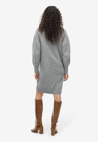 Vestito a maglione grigio a maniche lunghe, con orlo a costine e vestibilità comoda, abbinato a stivali di pelle marroni al ginocchio.