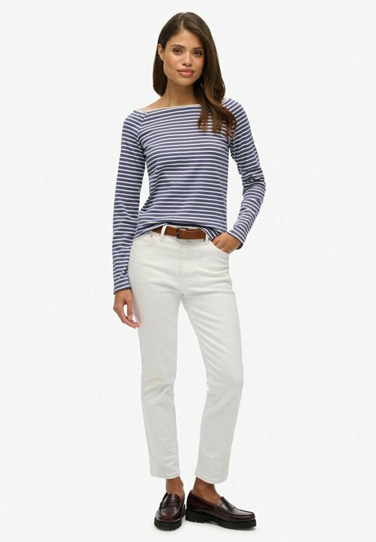 Camisa de rayas azul y blanca de manga larga, pantalones blancos ajustados, cinturón marrón y mocasines oscuros. Tejido suave, corte relajado y estilo casual.