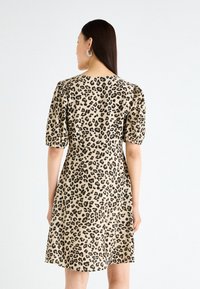 Leopard print dress in beige and black. Short puff sleeves and a fitted waist. Smooth fabric with a knee-length hem.