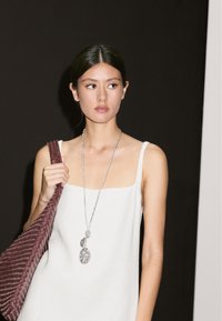 Weißes ärmelloses Oberteil mit quadratischem Ausschnitt, silberne Anhängerhalskette und eine bordeauxfarbene gewebte Tasche mit strukturierter Musterung.