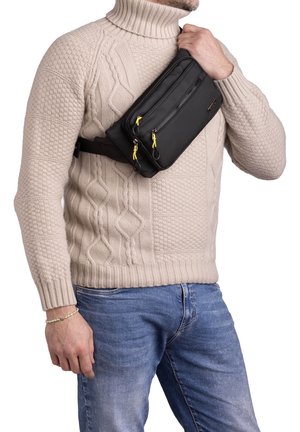 Borsa a tracolla nera con compartimenti doppi con cerniera, tiranti gialli e una texture liscia, indossata a tracolla sopra un maglione di maglia.