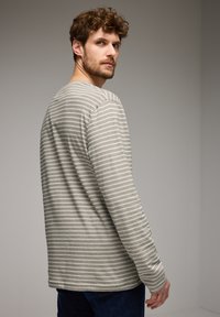 Svetr s dlouhým rukávem v světle šedé barvě s černými pruhy, kulatým výstřihem a měkkou texturou. Volný střih s přímými dlouhými rukávy.