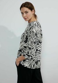 Top a maniche lunghe bianco e nero con un motivo floreale a foglie, dal taglio morbido e scollatura rotonda. Il tessuto sembra leggero.