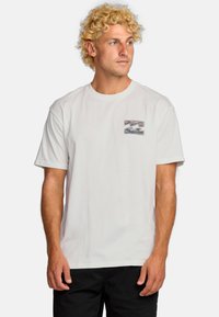 Hvid bomulds T-shirt med et lille, farverigt bølgedesign på venstre bryst. Kortærmet og med rund halsudskæring.