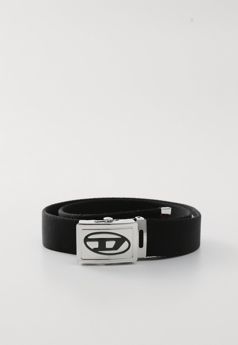 Μαύρη ζώνη από ύφασμα με ασημένια μεταλλική πόρπη που φέρει κυκλικό λογότυπο. Η ζώνη είναι λεία, επίπεδη και έχει στιβαρή σχεδίαση.