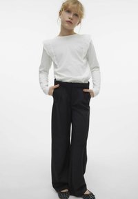 Biała bluzka z długim rękawem i koronkowym wykończeniem na ramionach, w połączeniu z czarnymi, wysokim stanem szerokimi spodniami i czarnymi butami na slip-on.