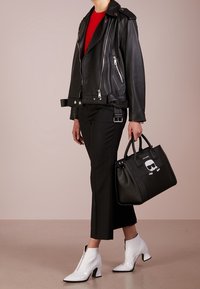 Mustat nahkainen moottoripyörävuori, punainen toppi, mustat lyhyet housut, valkoiset korkokengät. Musta laukku, jossa on graafinen painatus ja kaksoiskahvat. Sileät pinnat.