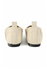 Pair of beige leather flat shoes with gathered sides and black soles, viewed from the back on a white background.