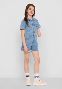 Robe en denim bleu clair avec des manches courtes, poches avant et une taille ceinturée. Accompagnée de baskets légères et de chaussettes à motifs.