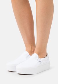 Scarpe slip-on bianche in tela con suola piatta in gomma bianca spessa e dettagli elastici sui lati. Design minimalista, senza pattern visibili.