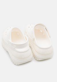 White Crocs clogs with a closed heel, ventilation holes, and a textured footbed. The sole is thick with a treaded pattern for grip.