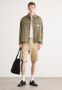 Olivengrønn skjortejakke, hvit t-skjorte, beige shorts, svart totebag, svarte sko, hvite sokker. Enkel design, bomullsstoff, uformell stil.