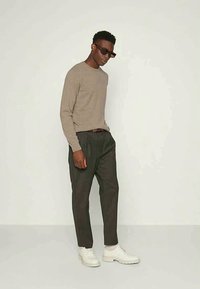 Καφέ μακρυμάνικη μπλούζα συνδυασμένη με σκούρους παντελόνες και λευκά αθλητικά παπούτσια. Τα αξεσουάρ περιλαμβάνουν σκούρα γυαλιά ηλίου και μια ζώνη με σχέδιο.