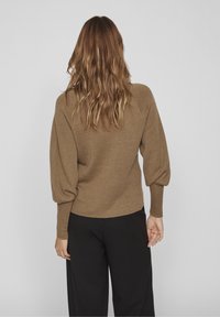Pull-over tricoté marron avec une finition texturée, doté de manches bouffantes et d'une coupe décontractée ; porté avec un pantalon noir ample.