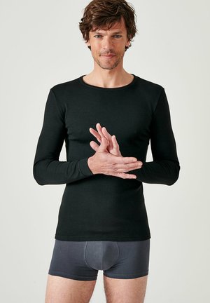 Zwarte longsleeve shirt met een ronde halslijn, gemaakt van gladde stof. Draagt over grijze boxershorts, met een aansluitend ontwerp.