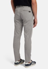 Helle graue Chinos mit slim Fit, ausgestattet mit Gesäßtaschen, Gürtelschlaufen und umgeschlagenen Säumen, kombiniert mit navyblauen und weißen Sneakers.
