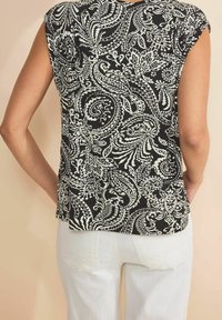 Černobílý top s paisley vzorem a krátkými rukávy, s polopřiléhavým střihem a zaobleným lemem, doplněný o bílé kalhoty.