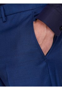 Navy blue fabric trousers with a textured finish, featuring a side pocket and a close-up of a hand placed inside.
