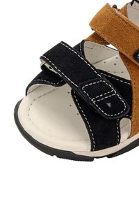 Sandalini per bambini realizzati in materiali scamosciati blu navy e marroni, con cuciture bianche, fasce in Velcro e soletta imbottita bianca. Suola in gomma nera.
