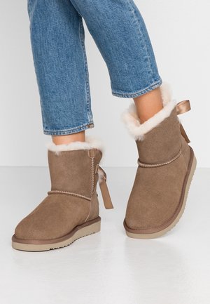 Enkellaarsjes van beige suède met witte fleece voering, gedragen met cropped blauwe spijkerbroek op een witte vloer.