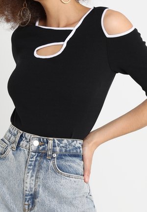 Top negro de canalé con cortes en los hombros y un detalle en la parte delantera tipo ojal, acentuado por ribetes blancos. Combinado con pantalones cortos de mezclilla claros de cintura alta.