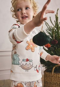 Children's cream sweatshirt with holiday-themed prints including gingerbread cookies, Christmas trees, and pudding. Soft fabric, long sleeves.