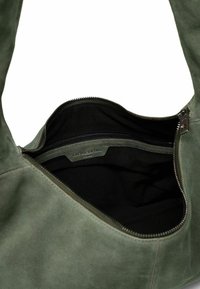 Borsa a spalla in suede verde oliva con chiusura a zip. Presenta un interno in tessuto nero e una piccola tasca interna con zip. Logo visibile all'interno.