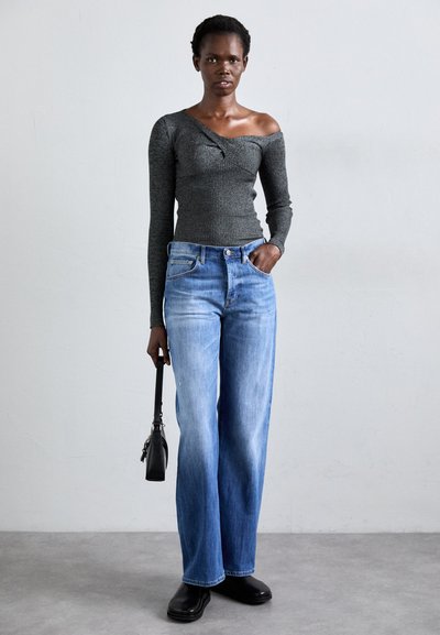 Gray ribbed long-sleeve top with an off-shoulder design, paired with light blue wide-leg jeans and black ankle boots, holding a black handbag.