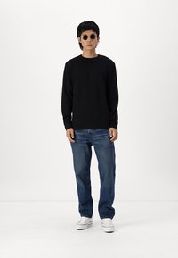 Černé tričko s dlouhým rukávem v kombinaci s džíny a bílými teniskami. Klasické sluneční brýle dotvářejí ležérní outfit. Jednoduchý design.