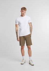 T-shirt blanc à manches courtes associé à un short marron. Le short est doté de poches latérales et d'une coupe décontractée. Les chaussures sont des baskets blanches et grises.