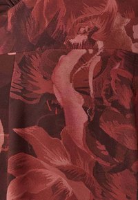 Röd tyg med blommönster i olika nyanser av vinrött och rosa. Har djärva blomformer och en mjuk, slät textur.