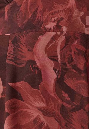 Röd tyg med blommönster i olika nyanser av vinrött och rosa. Har djärva blomformer och en mjuk, slät textur.