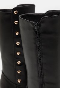 Bottes en cuir noir à la cheville avec fermeture éclair et accents métalliques en forme de cœur sur le côté. Texture lisse, design élégant.