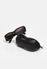 Bruņurupuču apļveida saulesbrilles ar tumšiem stikliem, taisnstūra forma, kopā ar melnu, ar rāvējslēdzēju aizveramu aizsargapvalku, uz kura ir redzams "vogue" zīmols.