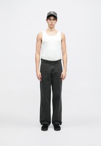 Biały top na ramiączkach, czarne szerokie spodnie i czarne sneakersy. Modelka nosi szaro-czapkę. Minimalistyczny styl na jednolitym białym tle.