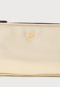 Χρυσό μεταλλικό πορτοφόλι με λεία υφή, διαθέτοντας ένα μικρό ανάγλυφο έμβλημα δύο πουλιών και φερμουάρ κατά μήκος της κορυφής.