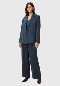 Donkerblauwe blazer op maat en bijpassende wijde broek van zachte stof. Bevat een notch-lapel, enkele knoopsluiting en zijzakken.