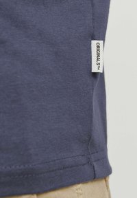 Marineblauw katoenen T-shirt met een label aan de zijnaad met de tekst "ORIGINALS." Heeft een ronde halslijn en korte mouwen. Zachte textuur.