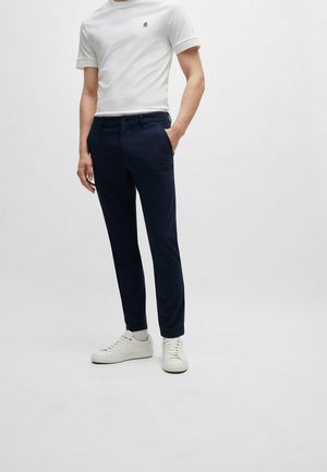 Witte korte mouwen shirt met geribde manchetten, marineblauwe broek en witte sneakers. De outfit heeft strakke lijnen en een minimalistisch ontwerp.